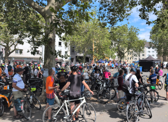 viele Radfahrende auf einem Platz, Im Hintergrund sind eine Bühne und Stände zu sehen.