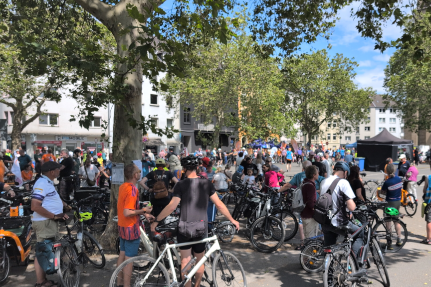 Duisburg_Ludgeriplatz.png viele Radfahrende auf einem Platz, Im Hintergrund sind eine Bühne und Stände zu sehen.
